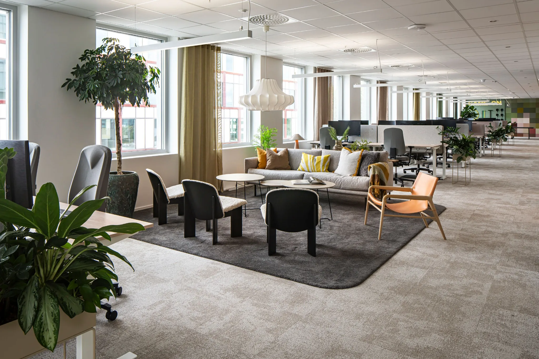 Lyst og fint kontorlandskap med detaljer som sofagruppe, planter og ergonomiske arbeidsplasser